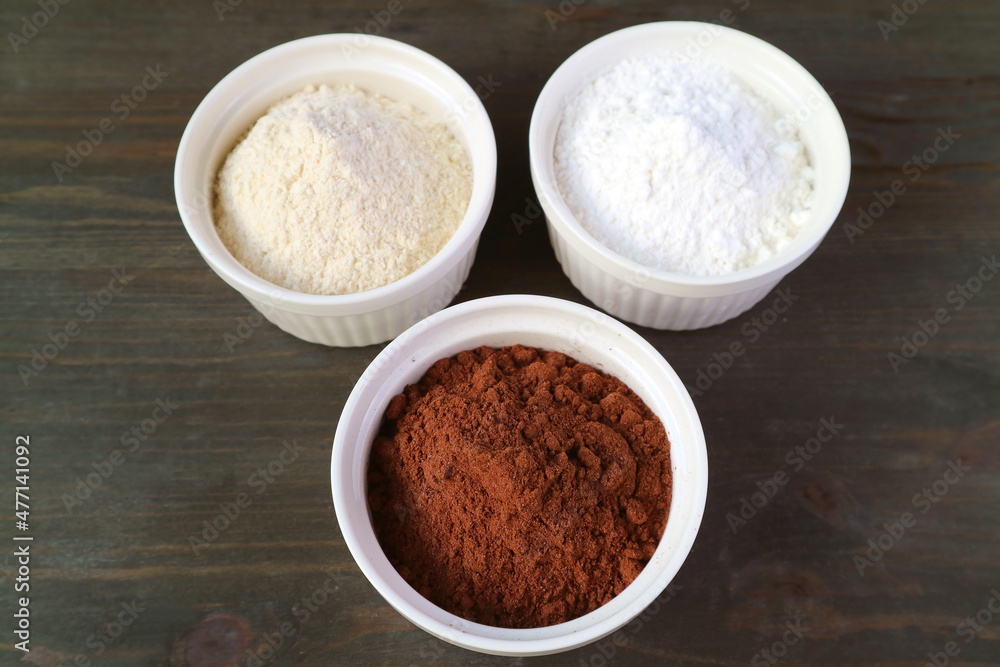 Closeup a Bowl of Cocoa Powder with Blurry Bowl of Whole-wheat Flour and White Flour on Black Wooden Table Closeup a Bowl of Cocoa Powder with Blurry Bowl of Whole-wheat Flour and White Flour on Black Wooden Table