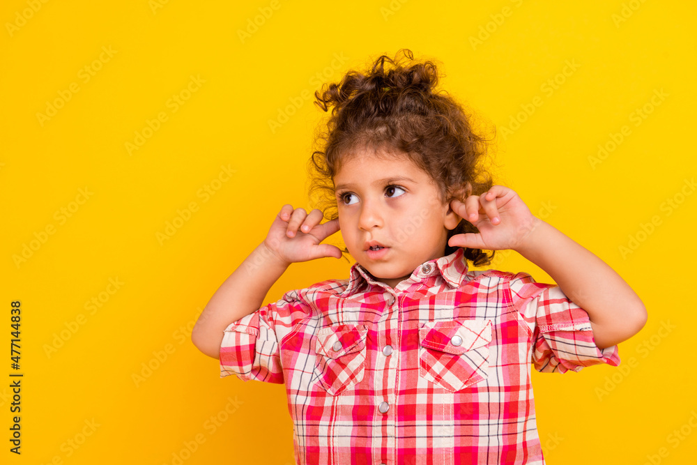 Photo of funny small bun brunette girl close ears look empty space wear red shirt isolated on yellow color background Photo of funny small bun brunette girl close ears look empty space wear red shirt isolated on yellow color background