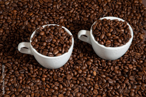 two cups of coffee on coffee beans on a brown background.