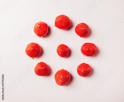 whole ripe strawberries laid out in a circle on a pink background, one strawberry in the center, top view