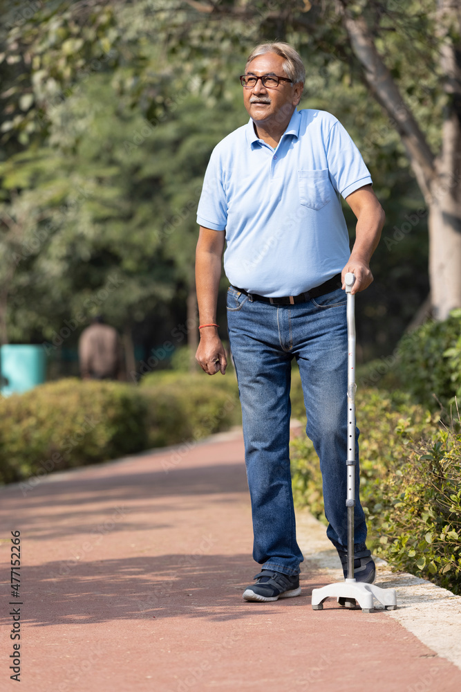 Senior man holding stick while walking at park Senior man holding stick while walking at park