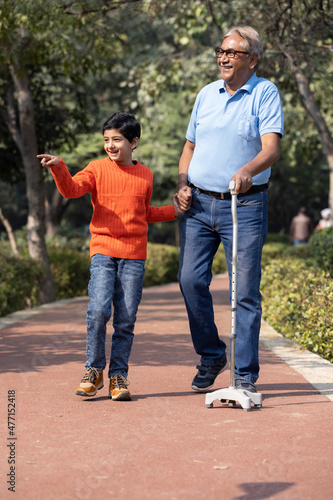 Senior man holding stick while walking with grandson at park 