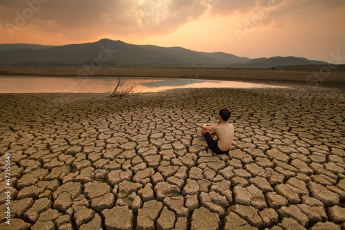 Fotografiet Young man sitting on dry cracked earth near drying river that impact by Drought