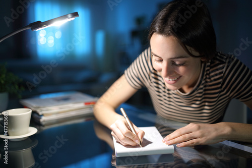 Happy woman taking notes in the night at home photo