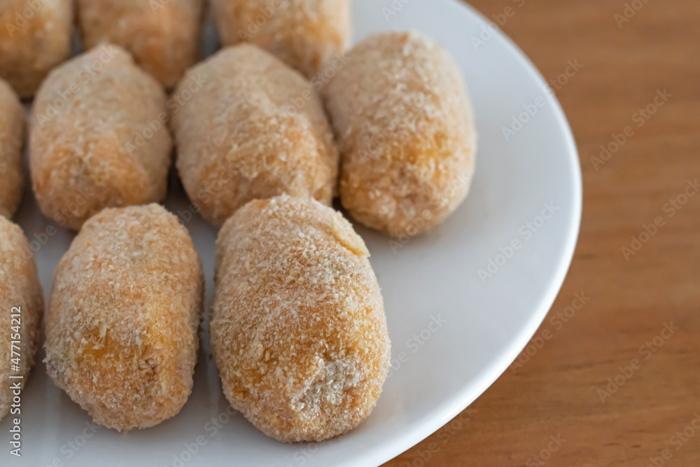Homemade croquettes ready for frying on white plate and wooden table Homemade croquettes ready for frying on white plate and wooden table