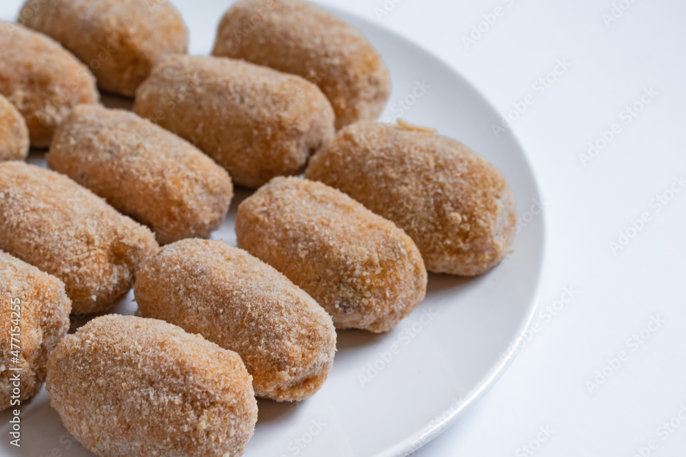 Homemade croquettes ready to fry. White plate and table. Homemade croquettes ready to fry. White plate and table.