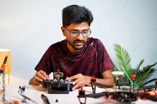 Obraz na plátne Young professional engineeer examining or testing drone configuration setting using remote control while repairning drone at shop - concept of uav or quad copter repair service and hobby