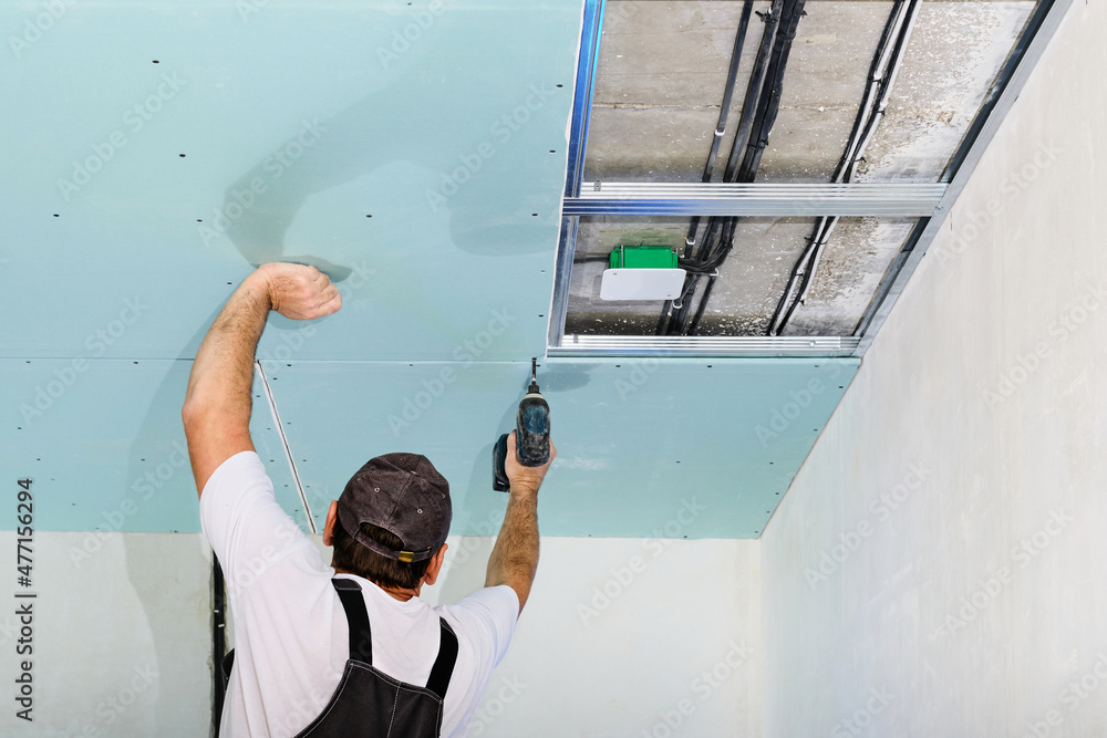 Foto Stock Mater is installing a plasterboard suspended ceiling. The