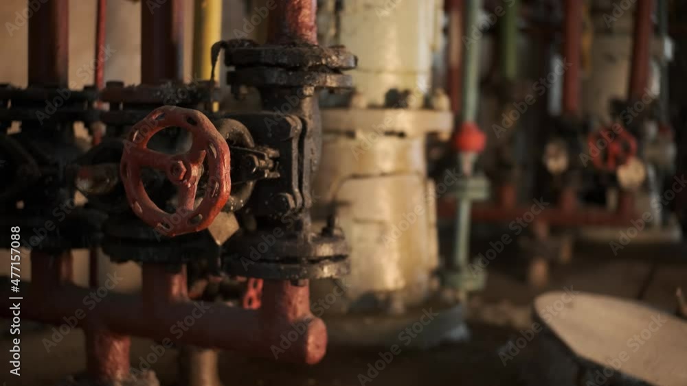 Old red valve at factory. many pipes and equipment in background. abandoned factory, sunlight from window falls on valve. Old red valve at factory. many pipes and equipment in background. abandoned factory, sunlight from window falls on valve.