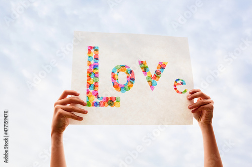 Hand of boy (8-9) holding colorful Love sign against sky