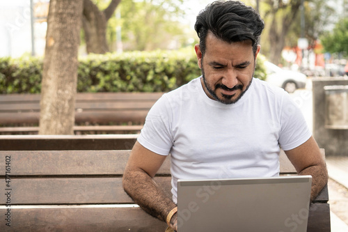 фотографія Latin man using his laptop on a plaza bench