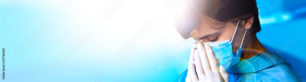 tired frontline young female doctor wearing protective medical face mask. close up blue uniform and gloves. Wide banner with copy space. health, medicine and pandemic concept