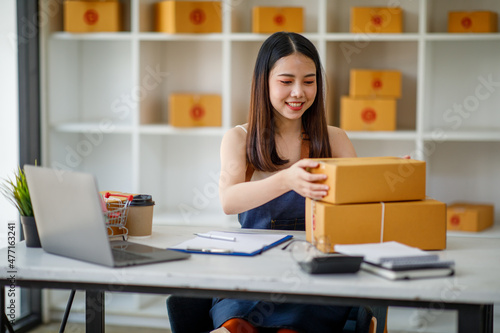 Startup small business entrepreneur SME or freelance woman using a laptop with box, AsianYoung woman seller prepare parcel box of product for delivery to customer Online selling e-commerce SME concept