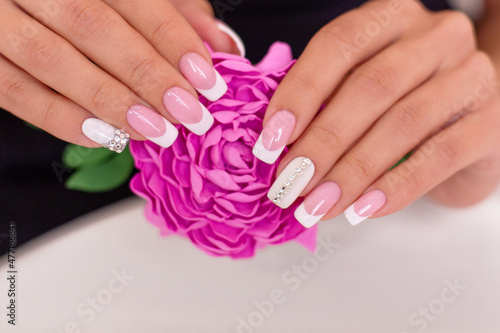 Close up view of beautiful female hands with luxury french manicure nails holding pink peony flower