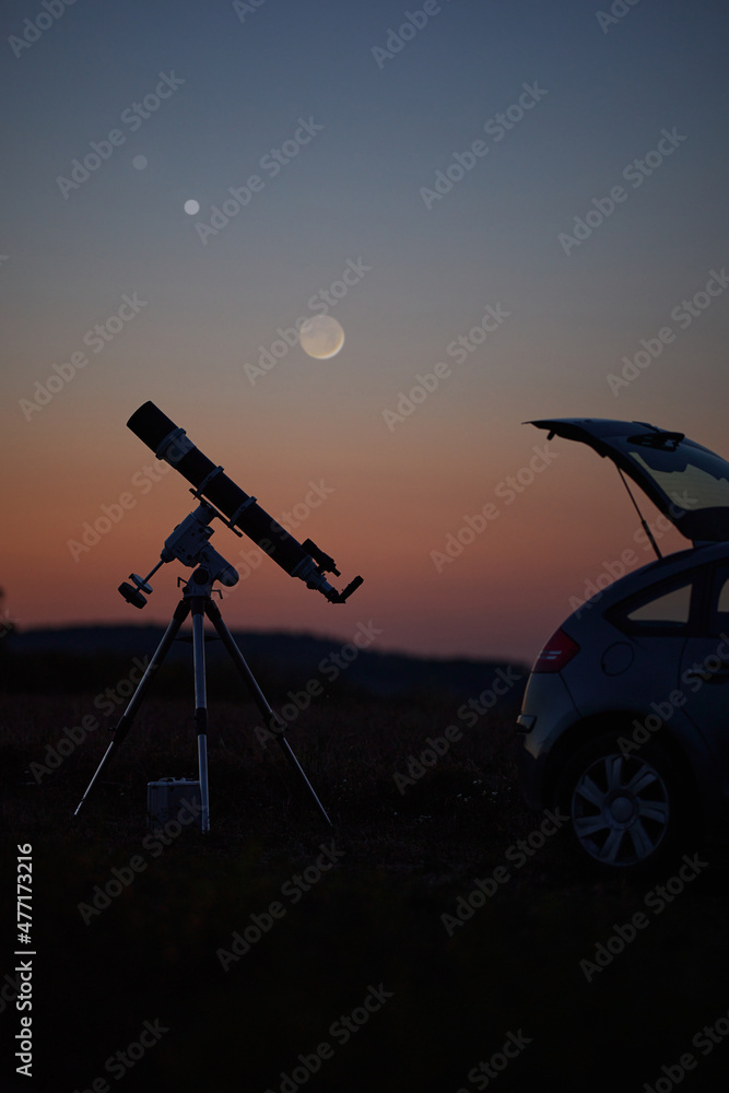 Silhouette of a car, telescope and countryside under the starry skies.