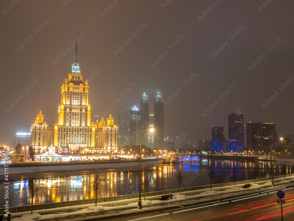 Fototapeta premium Illuminated high-rise stalinist building near river at winter night in Moscow, Russia. Historic name is Hotel Ukraine.