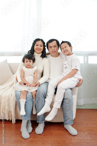Happy family with two kids sitting on sofa at home and looking at camera