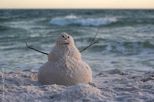 Tableau sur toile angry snowman or sandman with stick arms on the beach with oceans waves behind