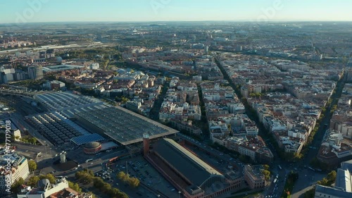 Forwards fly above urban neighbourhood. Large buildings of Atocha train station and traffic in streets around.