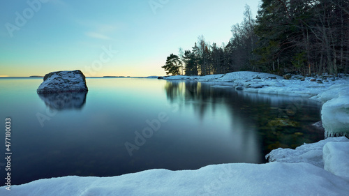 Before sunset at the end of winter in Uutela near Helsinki pretty snow-white ice floe melts against a backdrop of clear blue water and coastline.