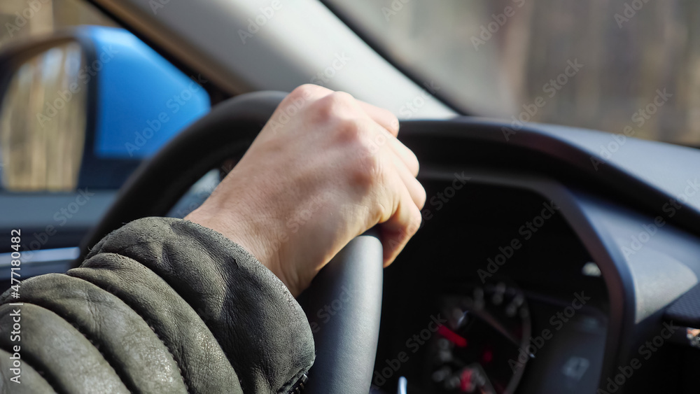 Man in dark warm sheepskin coat holds steering wheel confidently and drives foreign car along road between rows of trees in autumn forest closeup