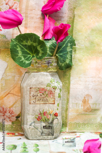 Glass jar, vase made by decoupage technique, fresh cyclamen flowers in it. Creativity, handmade background