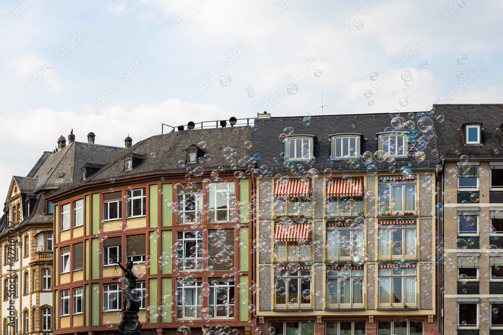 Viele Seifenblasen steigen vor einer Häuserfront in die Luft