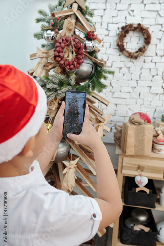 Boy photographing decorated Christmas tree on smartphone to post on social media