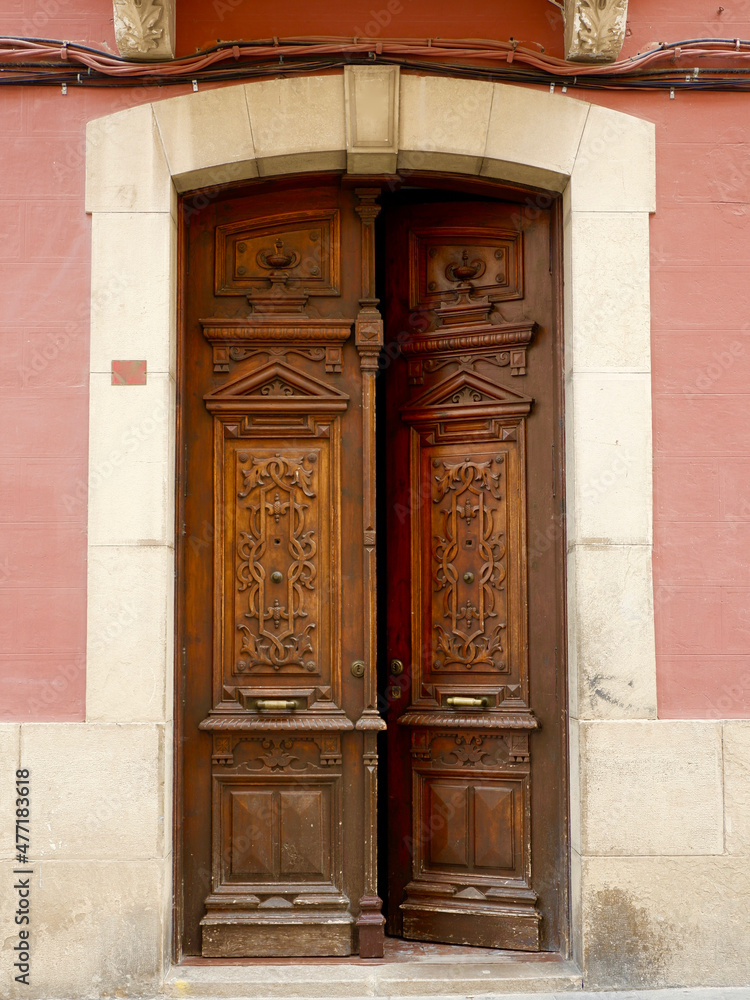 Classical double door made of warm red wood in Jaca, Huesca, Spain. Vintage entrance, classy antique details, floral curvy ornament