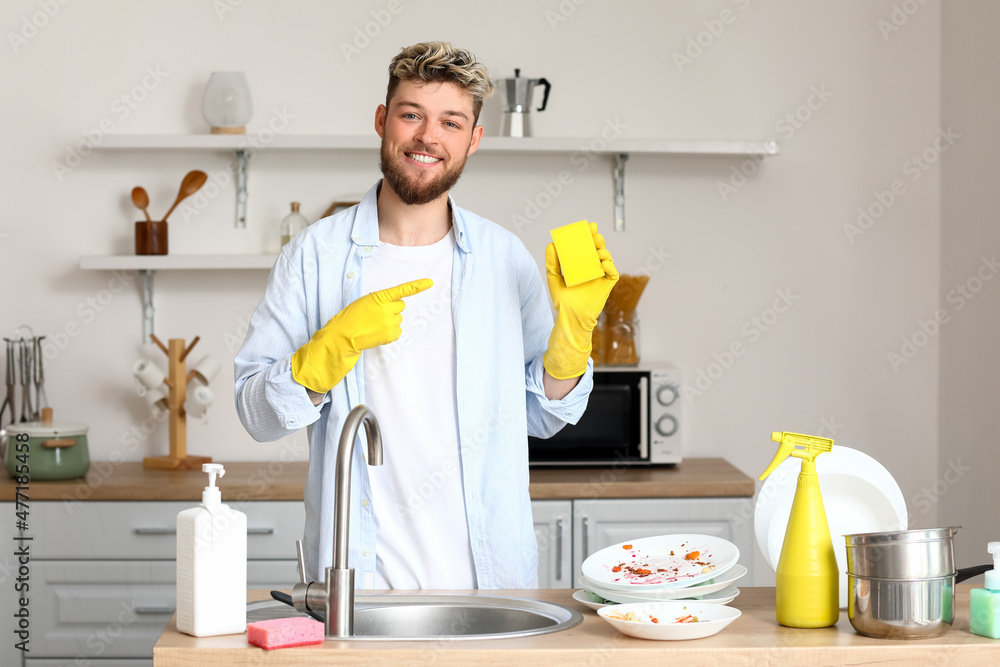 Handsome young man pointing at cleaning sponge in kitchen Handsome young man pointing at cleaning sponge in kitchen