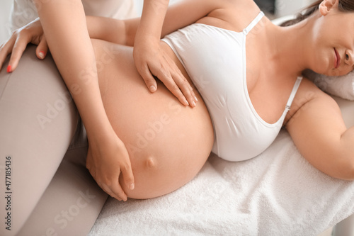 Pregnant woman getting massage by therapist in spa salon, closeup