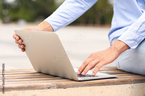 Young man using laptop on bench outdoors, closeup