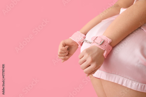 Young woman in handcuffs from sex shop on color background