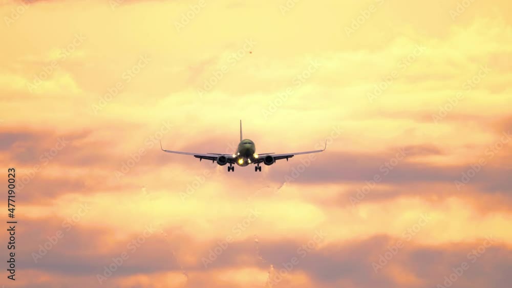 Silhouette of aircraft flying in orange sunset sky with clouds illuminated by setting sun. Gorgeous cloudscape with airplane. Flight of plane with flashing lights at sundown Silhouette of aircraft flying in orange sunset sky with clouds illuminated by setting sun. Gorgeous cloudscape with airplane. Flight of plane with flashing lights at sundown