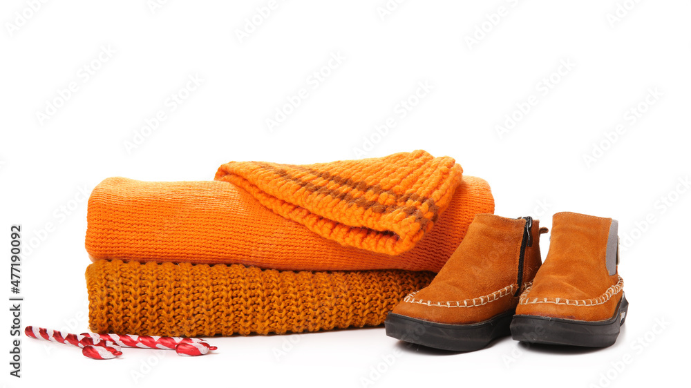 Stack of stylish sweaters, shoes, hat and candy canes on white background Stack of stylish sweaters, shoes, hat and candy canes on white background