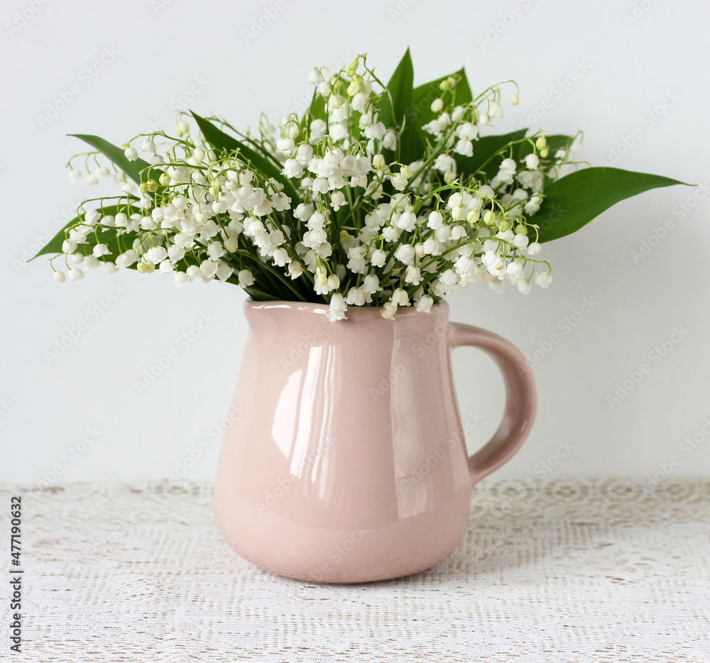 Fototapeta premium beige jug with a bouquet of lilies of the valley.