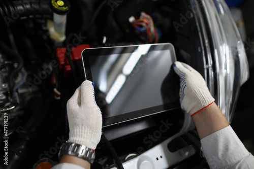 Man repairman holding digital tablet in front of open hood of car in garage closeup