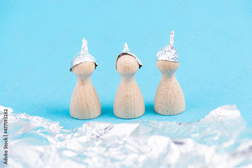 Three wooden figures wearing an alu hat, conspiracy theories, tin foil, symbolic Three wooden figures wearing an alu hat, conspiracy theories, tin foil, symbolic