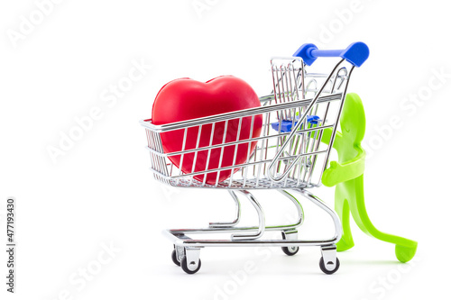 Green plastic toy abstract figure of man pushing shopping trolley with big red heart inside. Greeting card for Valentine's day. Ideas for healthcare, shopping in pharmacies or supermarket sales