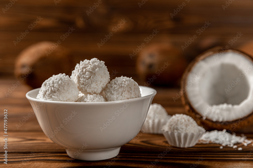 coconut candies in a bowl, coconuts on a wooden background. Close-up. coconut candies in a bowl, coconuts on a wooden background. Close-up.