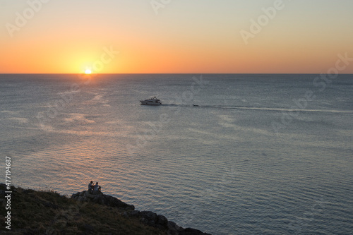 personas en la costa mirando el amanecer o atardecer con barco navegando