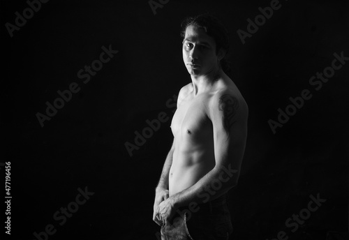 black and white low key portrait of shirtless man looking at camera black background