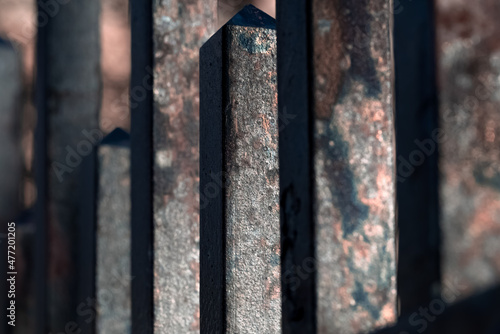 abstract closeup on a row of rusted metallic fence beams of alternating length with selective focus on a single surface standing out from the rest and creating a dramatic, grunge effect