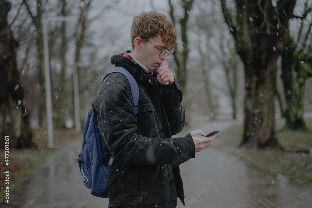 a young man stands in the middle of a park with an electronic cigarette and mobile phones a young man stands in the middle of a park with an electronic cigarette and mobile phones