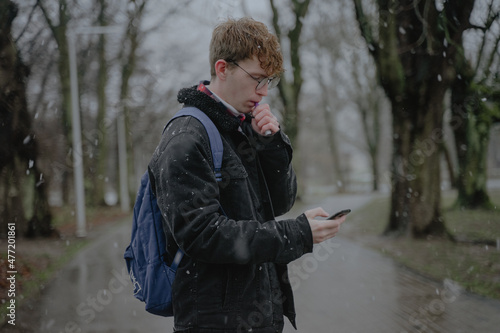 a young man stands in the middle of a park with an electronic cigarette and mobile phones © Maxim