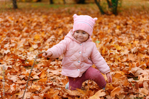 Child girl sitting on fallen leaves in autumn city park. Beautiful nature  trees with yellow leaves.