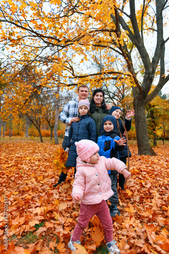 Portrait of a family with children in an autumn city park - happy people posing together near big tree, beautiful nature with yellow leaves as background.