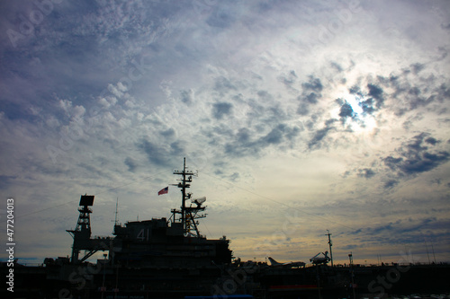 The Silhouette of the USS Midway Aircraft Carrier on the San Diego Embarcadero with Cloudy Skies and a Sun-flare in the Background © Gary Peplow