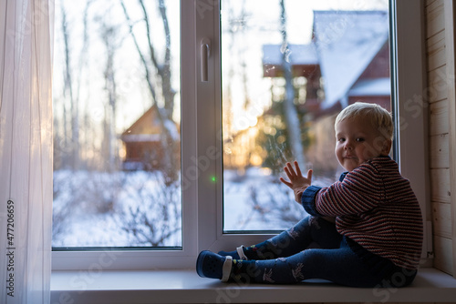 little boy stand near the window and look at the snowy street in winter, when it is very cold.