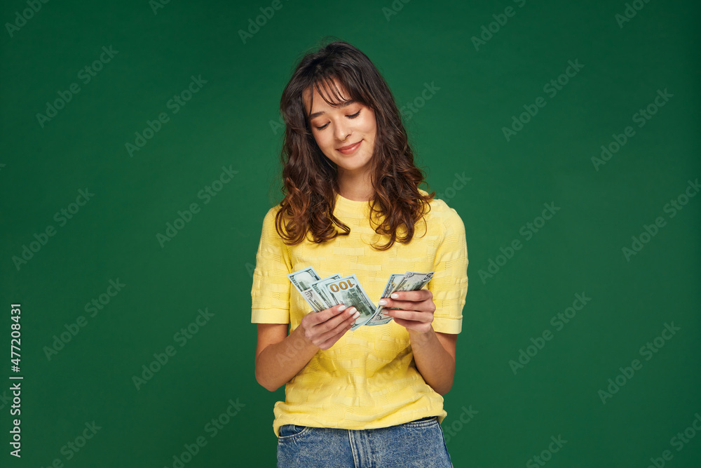 Modern satisfied young girl count cash money on green studio background. Financial fortune, success, payday